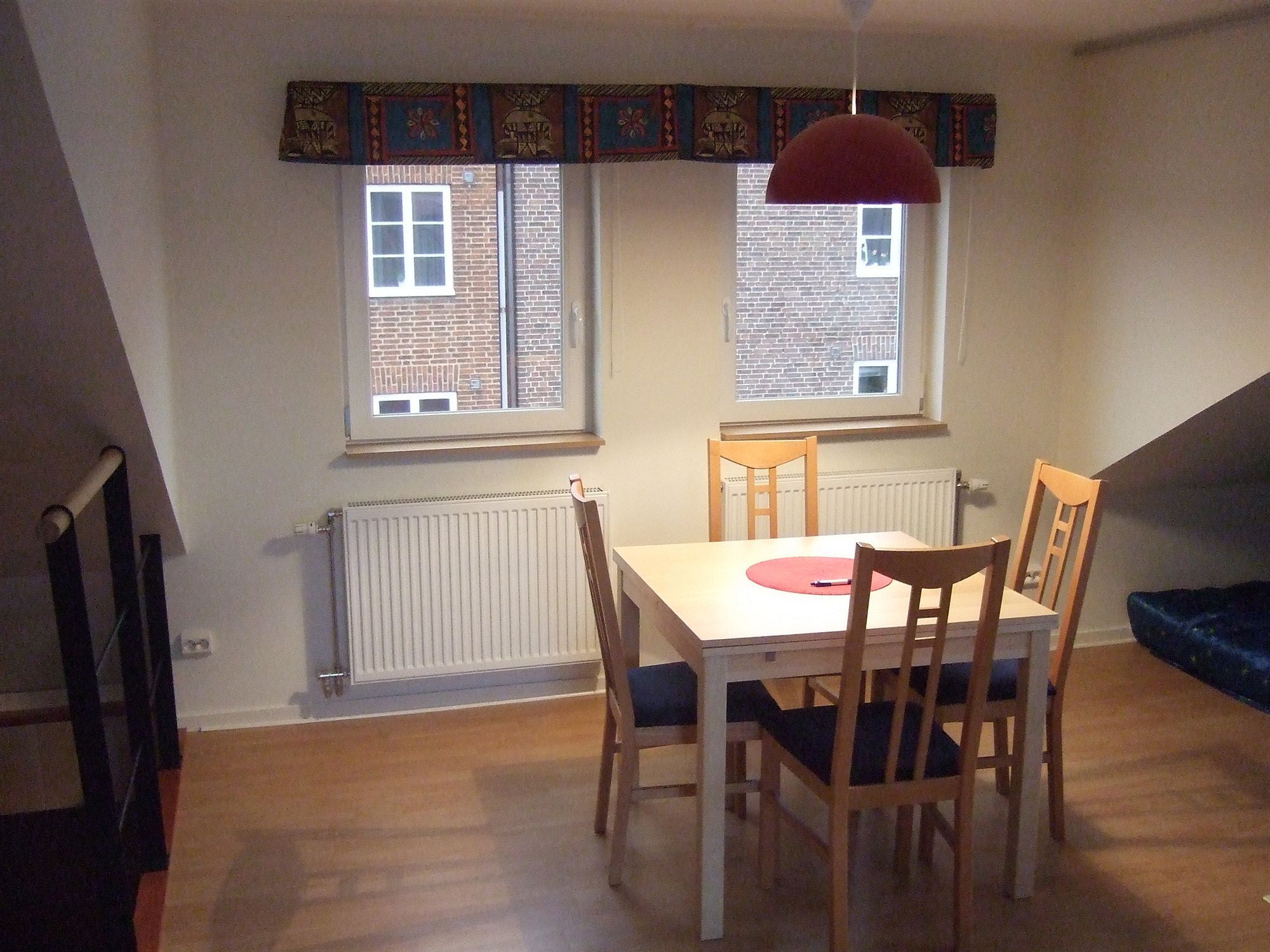 A dining area with a table and chairs, two windows with curtains, a radiator, and a hanging light fixture.
