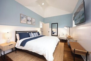 A bedroom with a bed, bedside tables, a chair, a bench, and artwork on the walls.