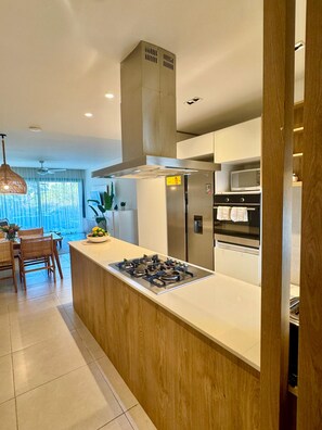 Eine moderne Küche mit einer zentralen Kochinsel, Edelstahlgeräten und einem Essbereich mit Holztisch und Stühlen.