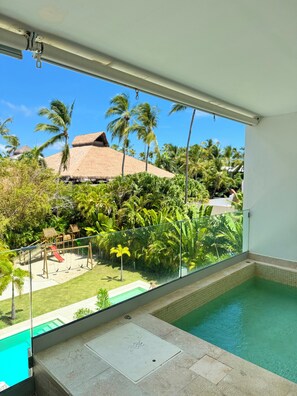 A balcony with a glass railing overlooking a swimming pool and a tropical garden. - PUNTA CANA OASIS WITH PRIVATE PICUZZI JUST A 2 MINUTE WALK FROM BAVARO BEACH! (Punta Cana)
