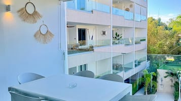 A modern outdoor dining area with a white table and chairs, a ceiling fan, and a view of a multi-story building with balconies.