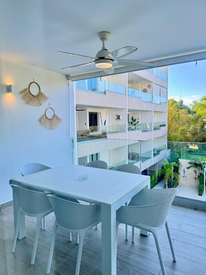 A modern outdoor dining area with a white table and chairs, a ceiling fan, and a view of a multi-story building with balconies. - PUNTA CANA OASIS WITH PRIVATE PICUZZI JUST A 2 MINUTE WALK FROM BAVARO BEACH! (Punta Cana)