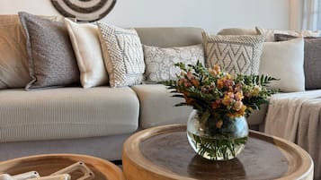 A living room with a sofa, decorative wall art, a vase with flowers, and a wooden table with a bone sculpture.