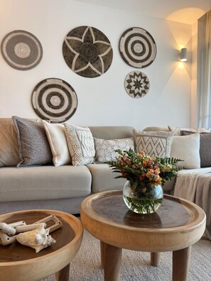 Un salon comprenant un canapé, des œuvres d’art décoratives accrochées au mur, un vase avec des fleurs et une table en bois sur laquelle est posée une sculpture en os.