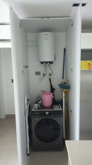 Ein kleiner Hauswirtschaftsraum mit Waschmaschine, einem rosa Eimer und einem Warmwasserbereiter.