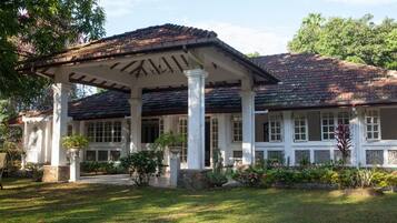 A building with a covered porch supported by columns, a tiled roof, and a well-maintained garden.
