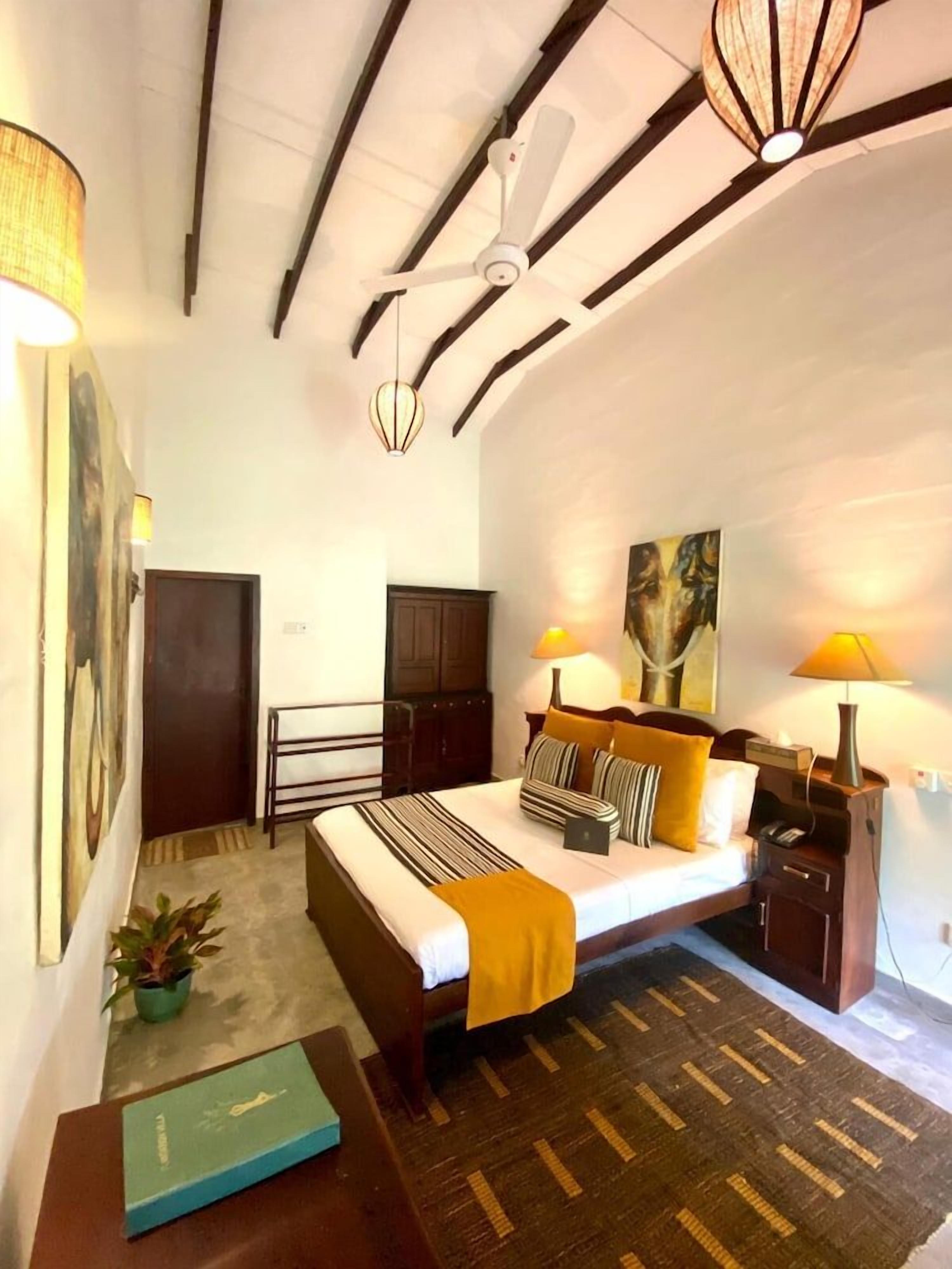 A bedroom with a bed, bedside tables, a ceiling fan, and a painting on the wall.