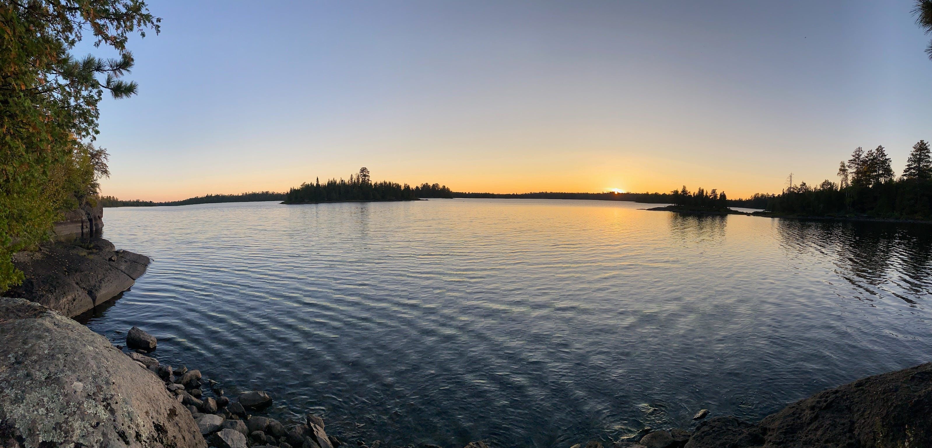 En stilla sjö med en stenig strand och träd i bakgrunden.