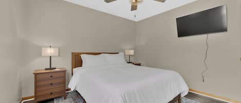 A bedroom with a bed, nightstands, a ceiling fan, a TV mounted on the wall, and a patterned rug.