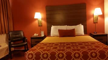 A hotel room with a large bed, two bedside lamps, a telephone, a chair, and a desk with a lamp.