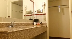 Een badkamer met een granieten aanrecht, een wastafel, een spiegel en twee haardrogers bevestigd aan de muur.