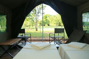 A tent with two beds, a table, and chairs, with a view of a grassy area and trees. - Big Game Camp Udawalawe (Sri Lanka)