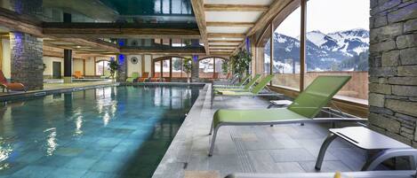 An indoor swimming pool with lounge chairs and a mountain view.