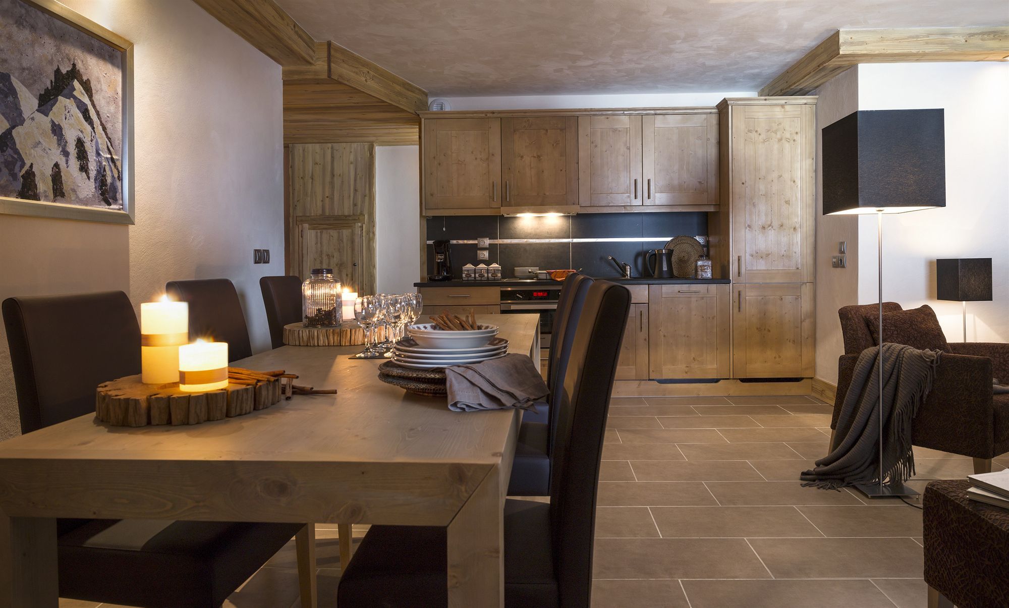 Un coin repas avec une table en bois, des chaises, des bougies et un tableau au mur.