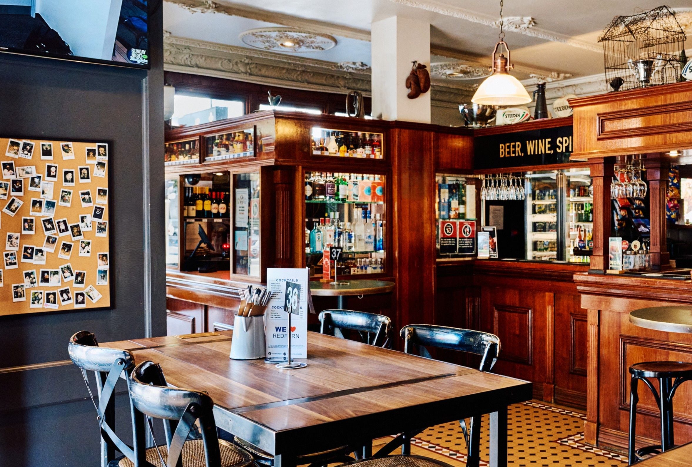 Una zona de bar con muebles de madera, una pizarra de menú y una pared con fotografías.