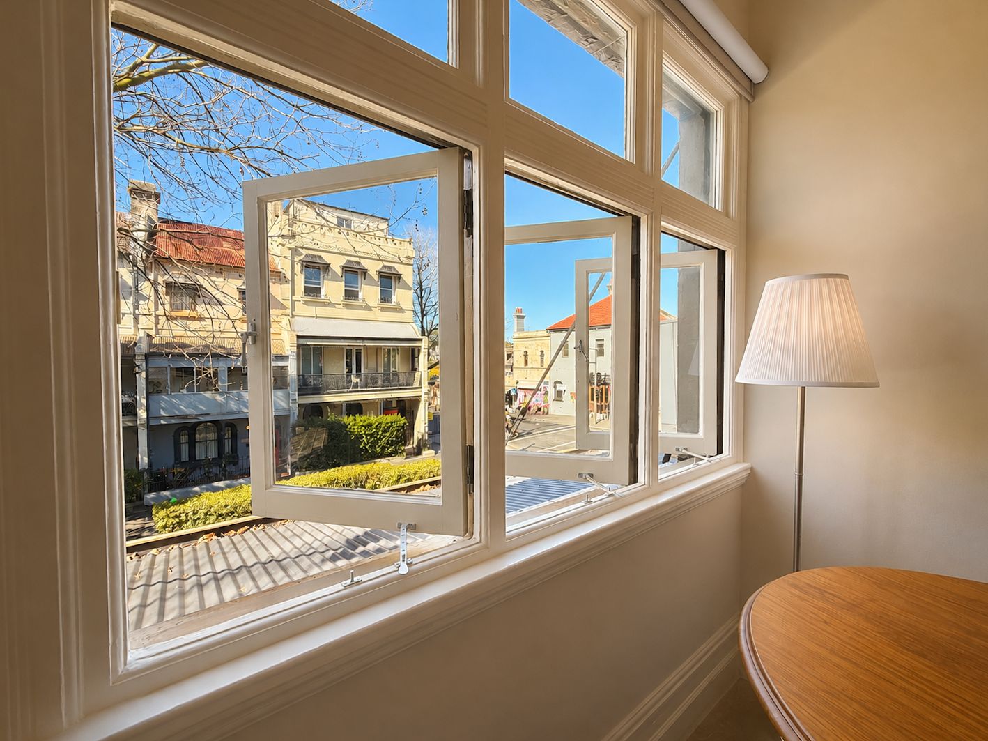 A room with a large window offering a view of a street with buildings and a lamp on a table.