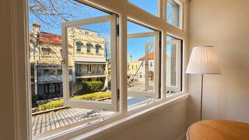A room with a large window offering a view of a street with buildings and a lamp on a table.