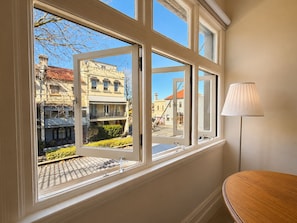 Una habitación con un ventanal que ofrece vista a una calle con edificios y una lámpara sobre una mesa.