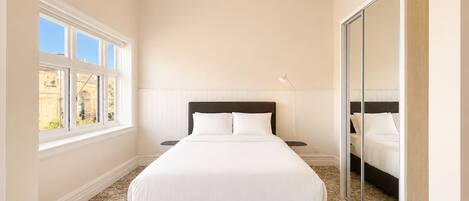 A bedroom with a large bed, a nightstand, a lamp, a window with multiple panes, and a mirror.