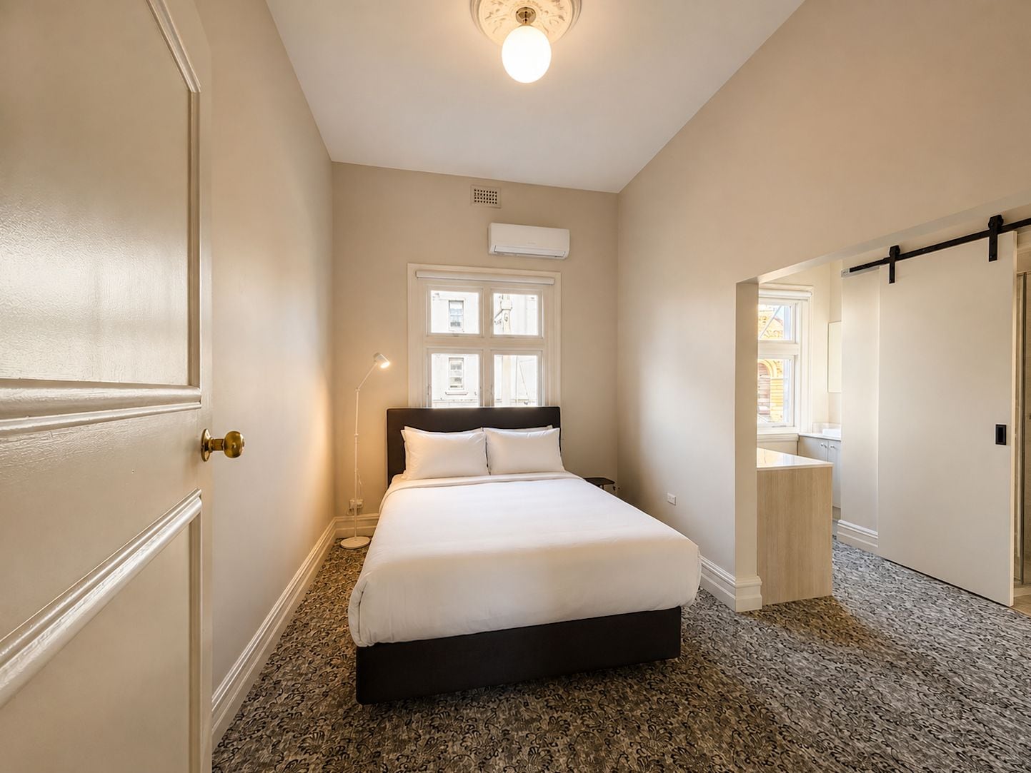 A bedroom with a bed, a window, an air conditioning unit, and a door.