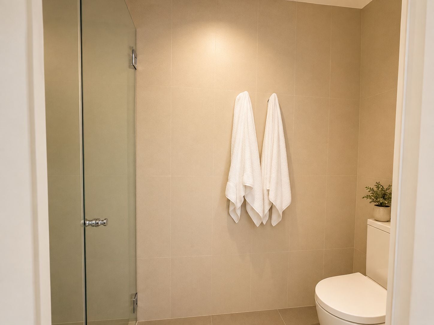 A bathroom with a toilet, a shower, and two towels hanging on the wall.