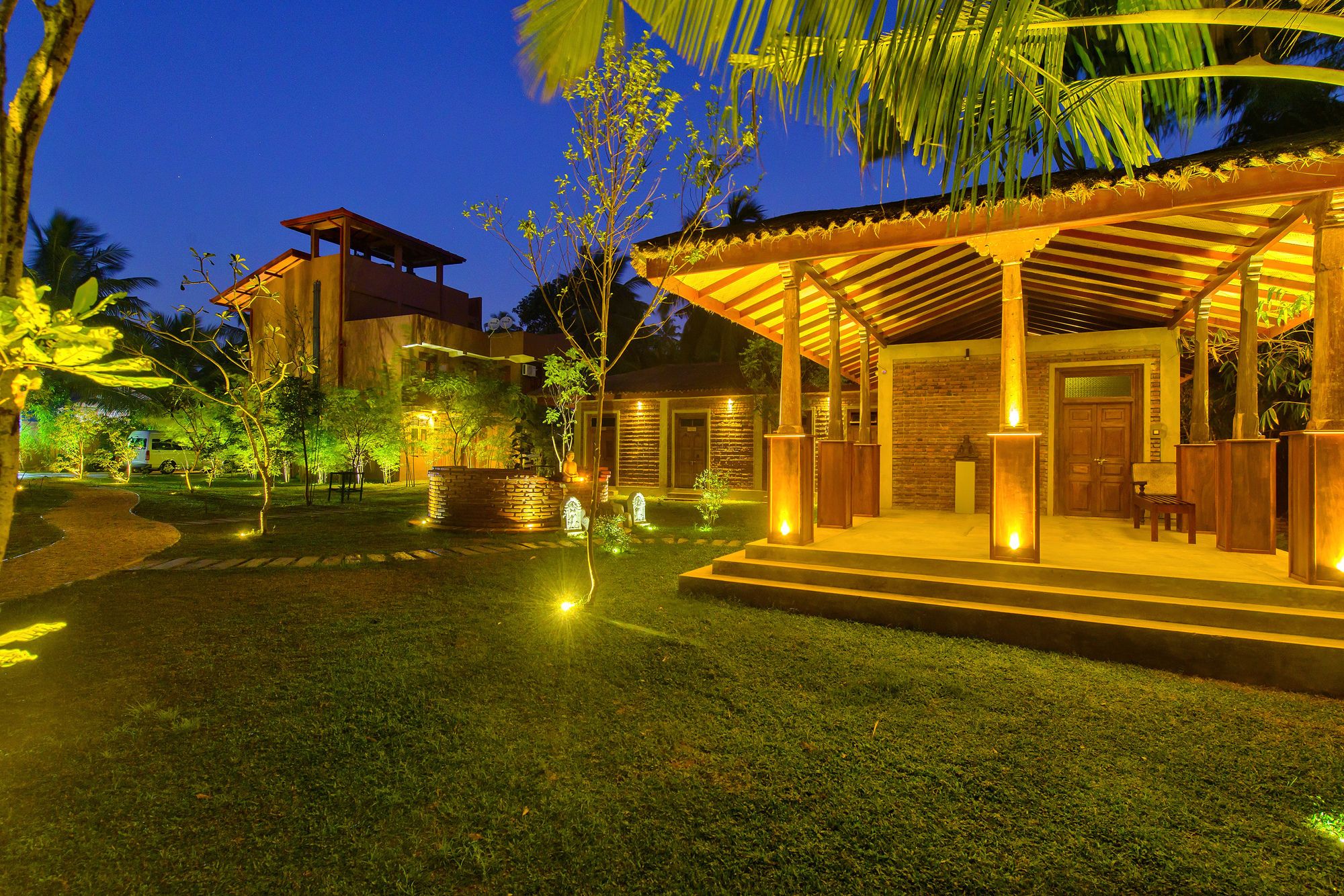 A well-lit outdoor area with a covered seating area, a stone building, and a pathway leading to a vehicle.