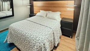 Un dormitori modern amb un llit gran, una capçalera amb lamel·les verticals, una taula de nit i un mirall.