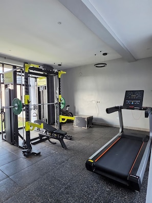 Ett gym med löpband, styrketräningsutrustning och en digital skärm som är monterad på väggen.