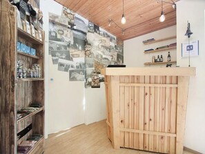 Una habitación con mostrador de recepción de madera, estantes con diversos objetos y una pared decorada con fotografías.