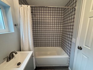Un baño con bañera, lavamanos y cortina de ducha de estampado geométrico.