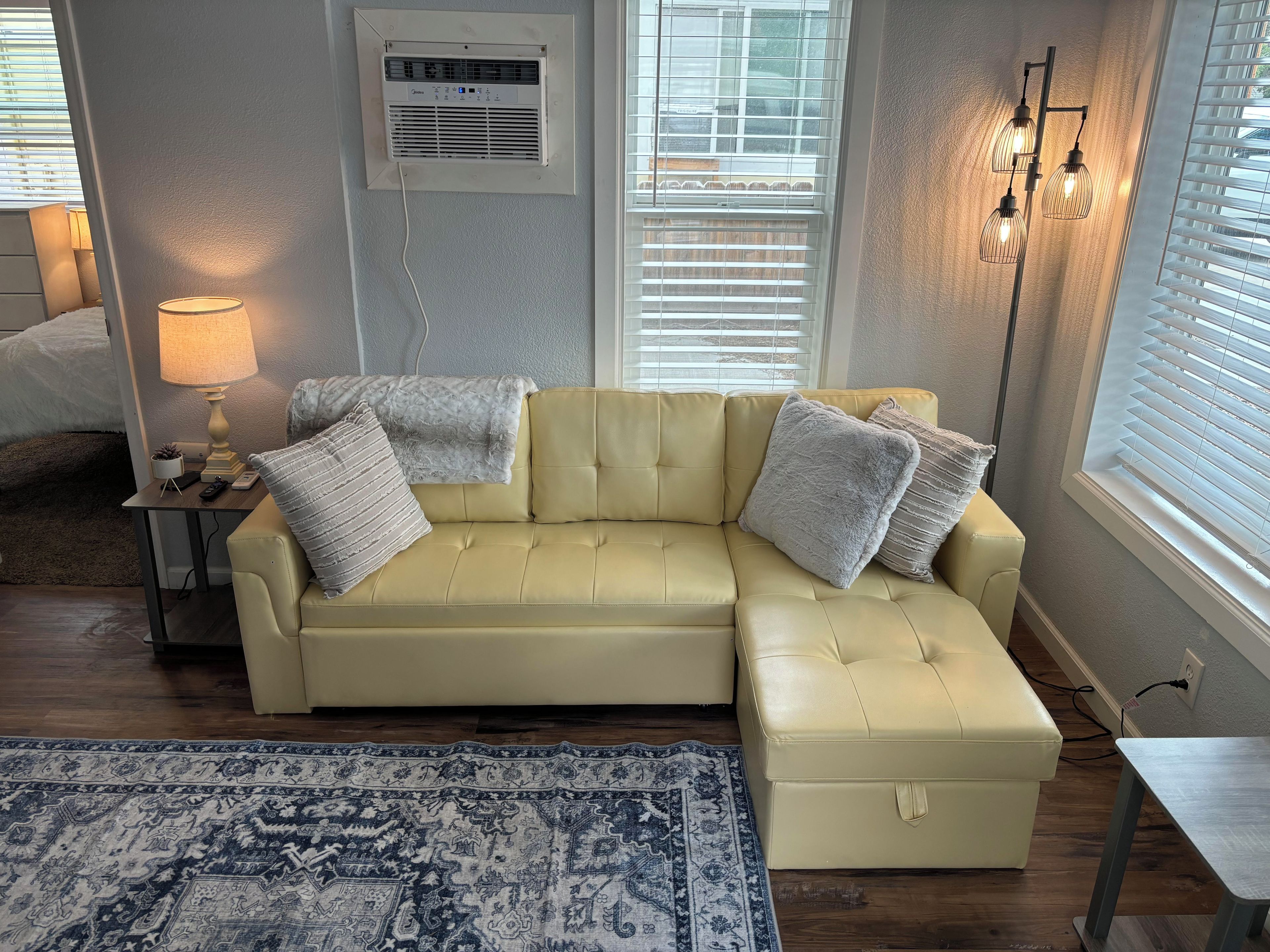 Une pièce avec un canapé en cuir jaune, un tapis à motifs, une lampe et un climatiseur fixé au mur.