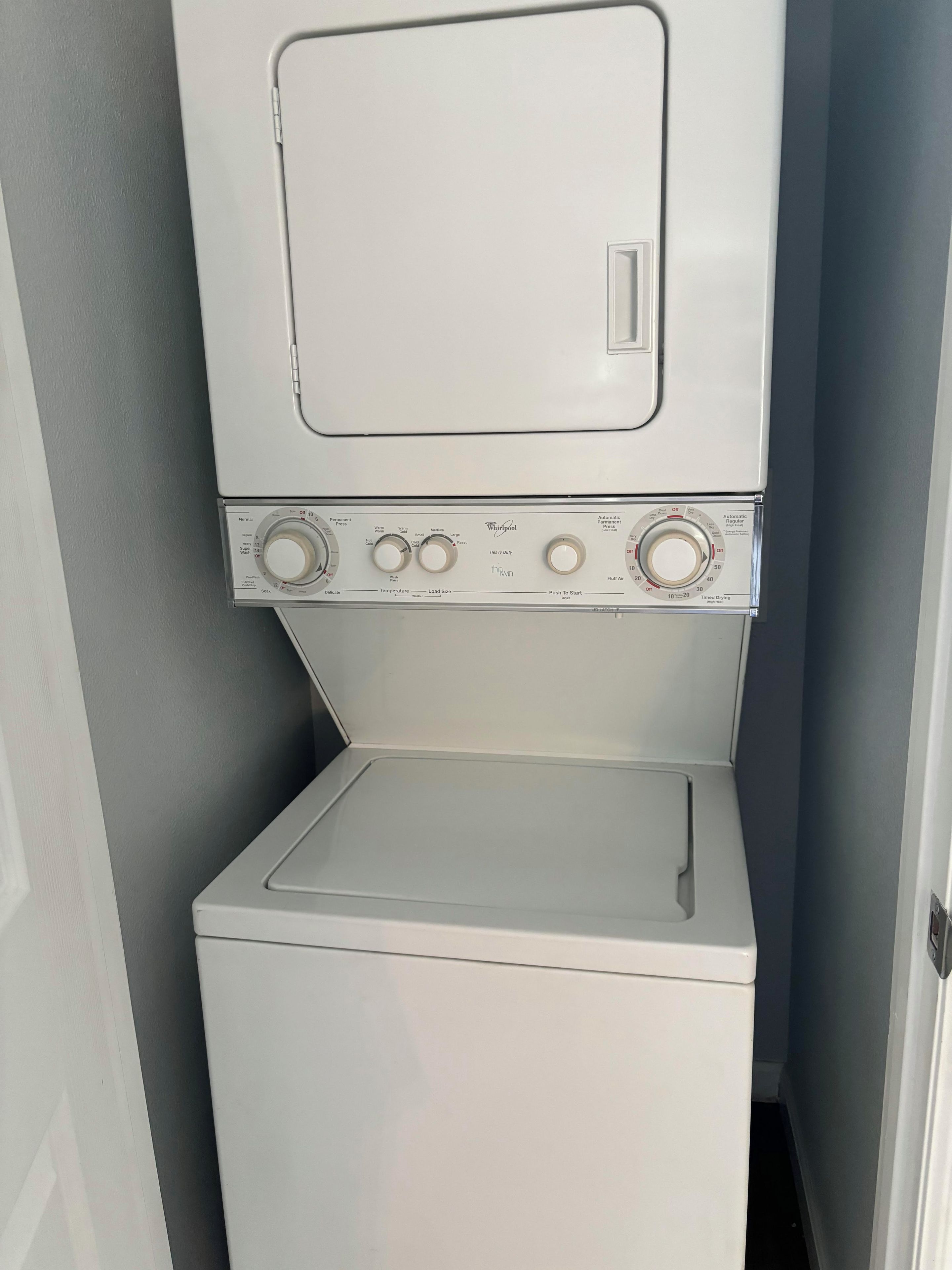 A front view of a stacked washer and dryer unit with control knobs and a door.