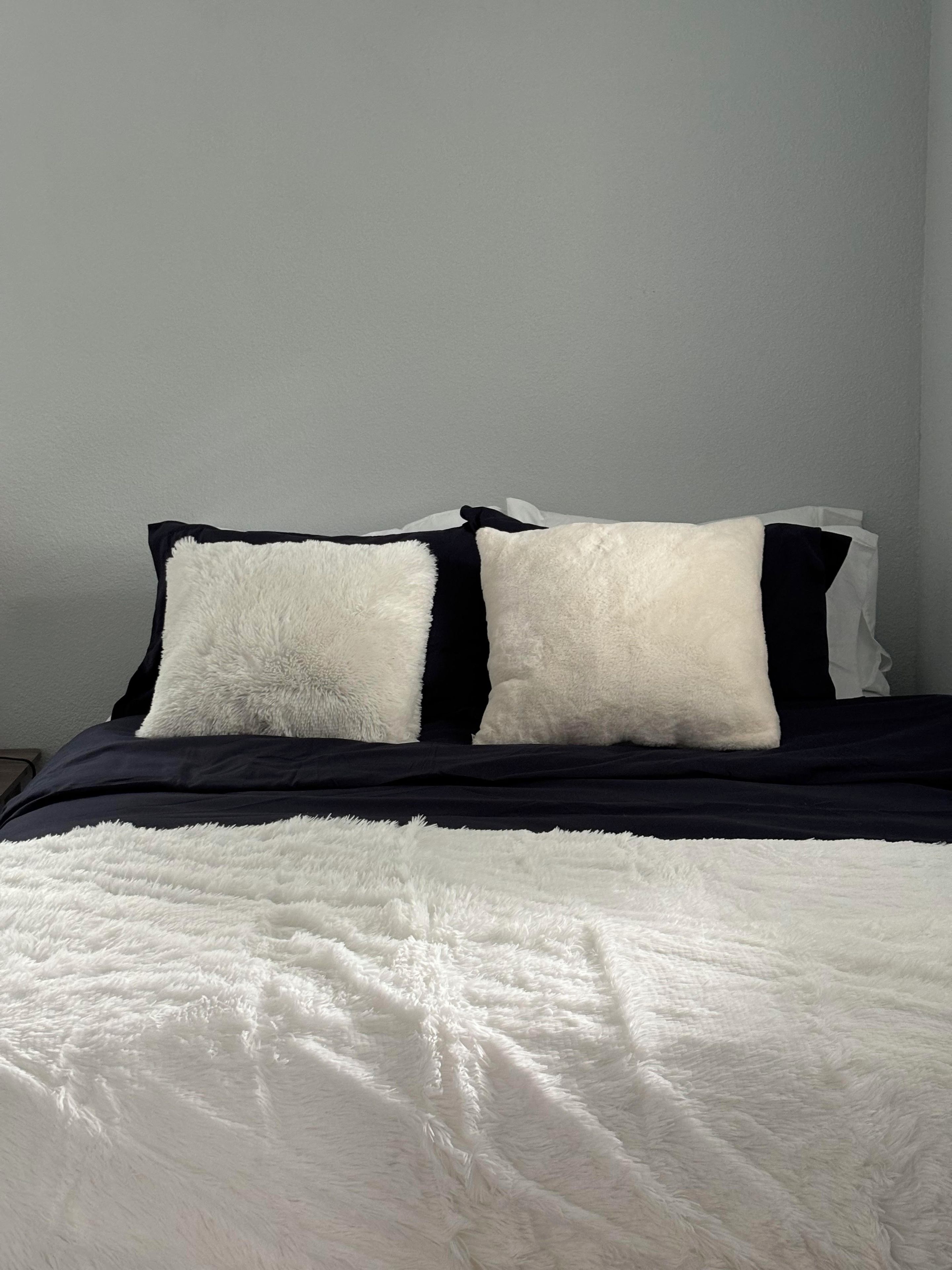 Una cama con un edredón blanco mullido y almohadas negras.