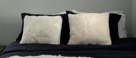 Una cama con un edredón blanco mullido y almohadas negras.