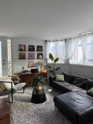 A living room with a sofa, a coffee table, a plant, and a wall with framed pictures. - Sunny Corner Heart Of Plateau (Montréal)