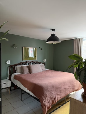 A bedroom with a bed, a bedside table, a lamp, a mirror, and a window with curtains. - Sunny Corner Heart Of Plateau (Montréal)
