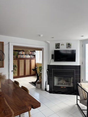 A modern living room with a fireplace, a flat-screen TV mounted above it, and a bookshelf filled with books. - Sunny Corner Heart Of Plateau (Montréal)