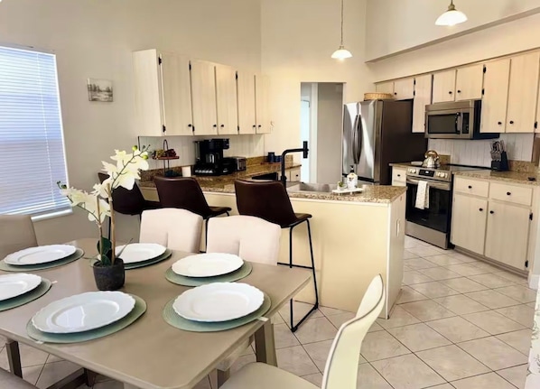 Una cocina moderna con armarios blancos, una isla central y un comedor con mesa dispuesta para cuatro.