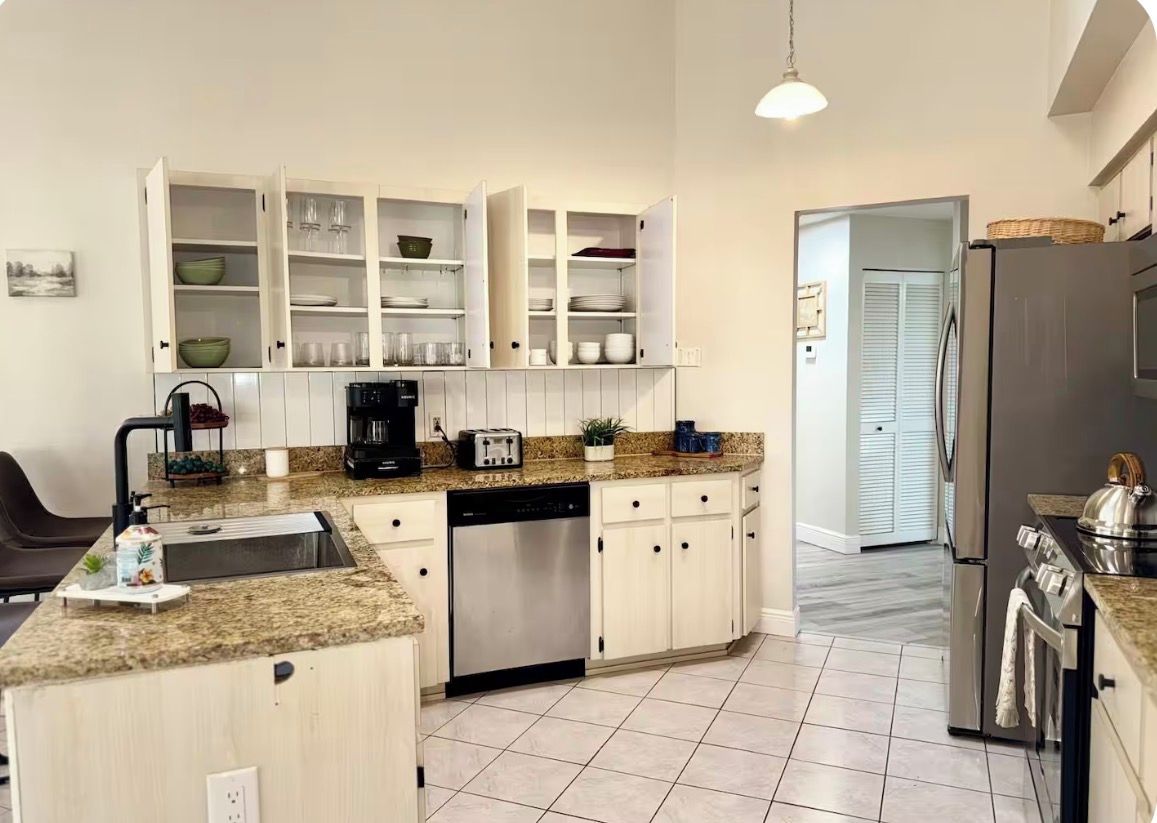 Una cocina moderna con armarios blancos, encimera de granito, lavavajillas integrado y refrigerador de acero inoxidable.