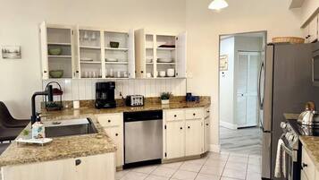 Una cocina moderna con armarios blancos, encimera de granito, lavavajillas integrado y refrigerador de acero inoxidable.