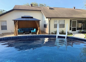 A residential swimming pool with a covered seating area and a house in the background. - Spring Hill Stay 
Pool, Games & Relaxation (Spring Hill)