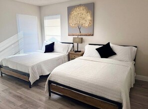 Un dormitorio con dos camas, una mesita de noche, una lámpara y un cuadro de un árbol.