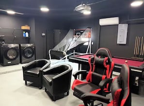 Habitación con mesa de billar, una silla gamer, lavadora y aro de baloncesto.