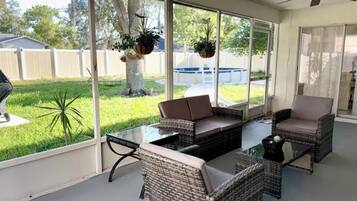 Un solárium con mobiliario de mimbre, ventanas amplias y vista al jardín trasero.