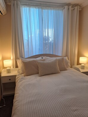 Ein Hotelzimmer mit einem großen Bett, zwei Nachttischen inklusive Lampen und einem Fenster mit durchscheinenden Vorhängen.