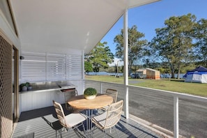 A covered outdoor area with a table and chairs, a small kitchen area, and a view of the surrounding landscape. - Reflections Holiday Park Ferry Reserve (Brunswick Heads)