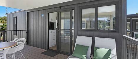 A balcony with a table and chairs, a sliding glass door leading to a room, and a view of the surrounding area.