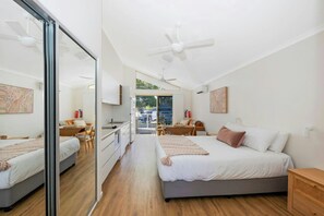 A modern bedroom with a large bed, a desk, and a chair, a bathroom with a shower, and a view of the outside. - Reflections Holiday Park Ferry Reserve (Brunswick Heads)