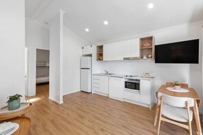 A modern kitchen with white cabinetry, a built-in oven, and a flat-screen TV mounted above the counter. - Reflections Holiday Park Ferry Reserve (Brunswick Heads)
