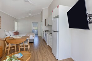 A modern kitchen with white appliances, a dining area with a wooden table and chairs, and a visible door leading to another room. - Reflections Holiday Park Ferry Reserve (Brunswick Heads)